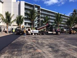 Asphalt paving in progress in front of a large white building with palm trees on a sunny day.