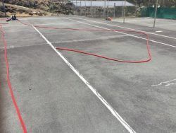 Red hoses on an asphalt tennis court, next to white painted lines.