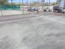 Tennis court with white lines, grey surface, and green net in the background.
