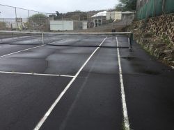 Wet tennis court with net, white lines, and surrounding fence.