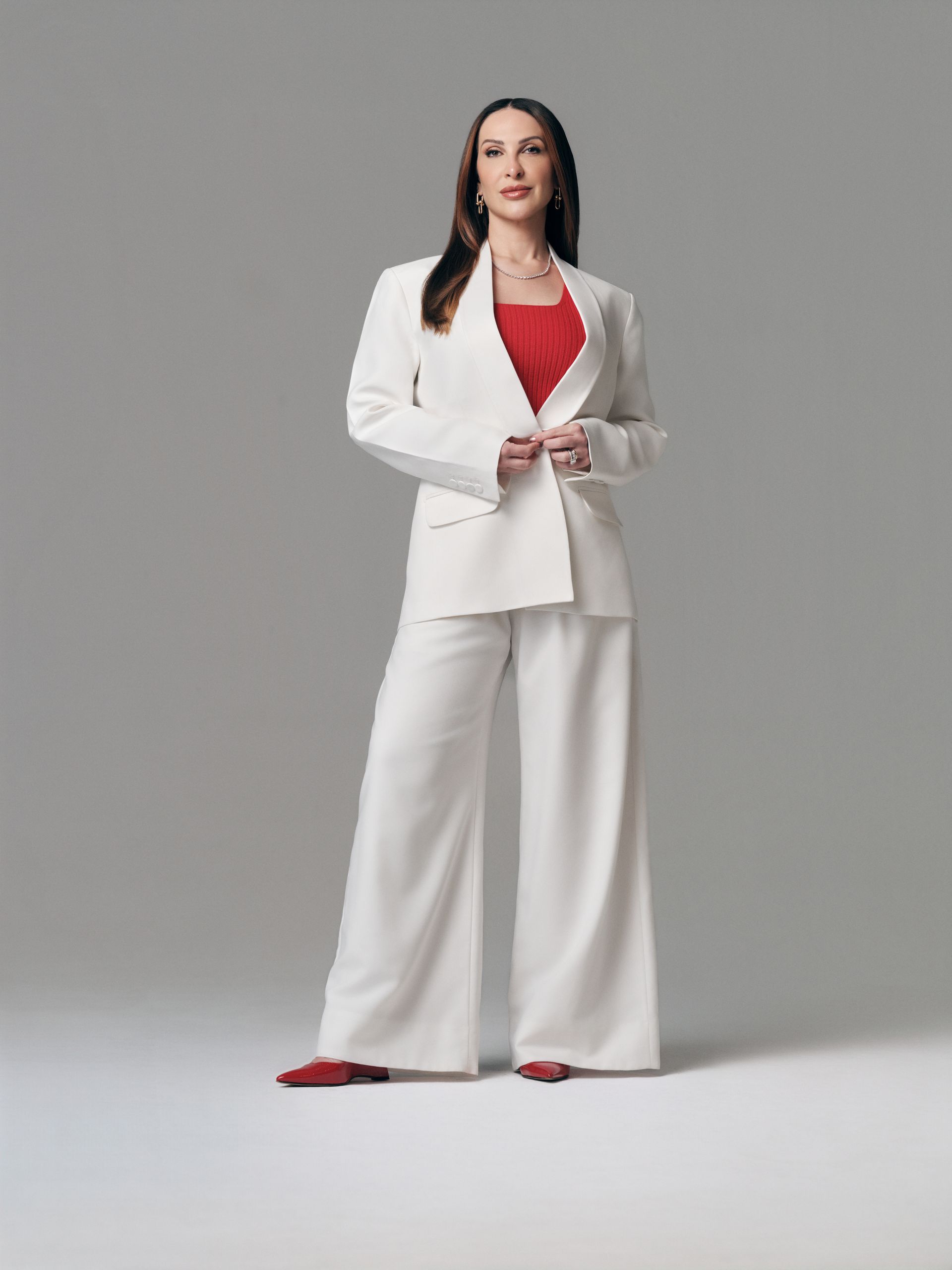 A doutora Kássila de terno preto e branco está de pé com os braços cruzados.