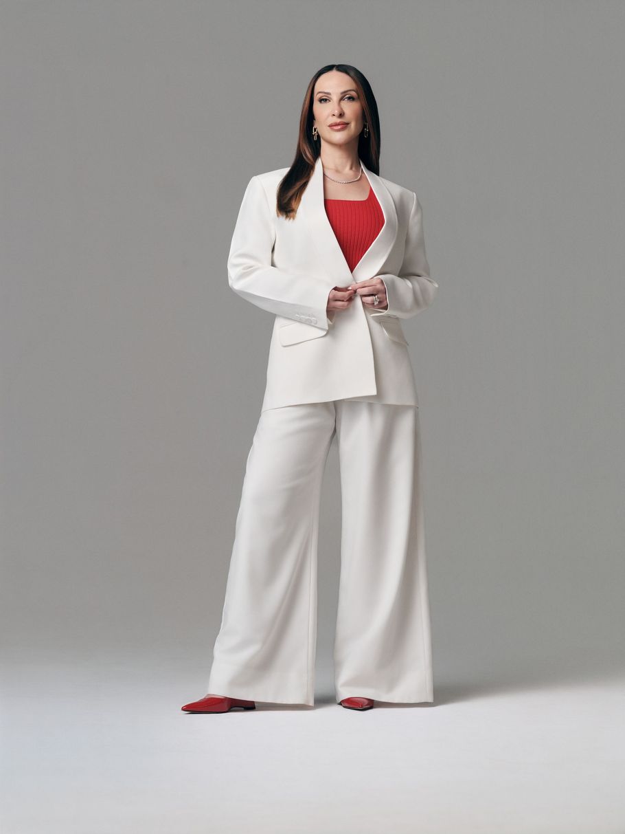 A doutora Kássila de terno preto e branco está de pé com os braços cruzados.