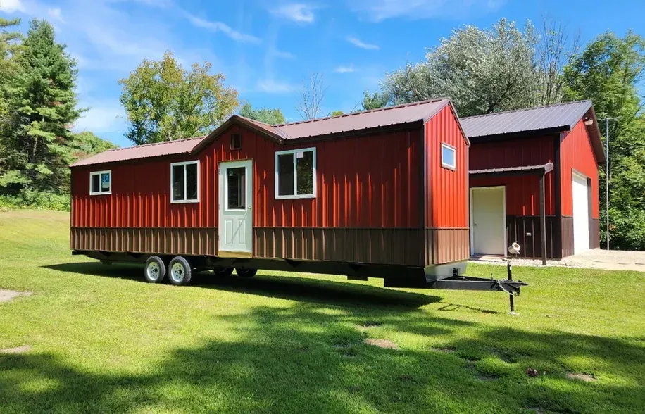 A red trailer is parked in front of a red barn.