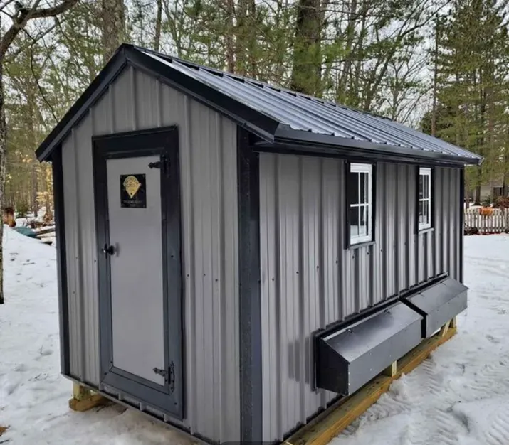 A gray shed with a black roof is sitting in the snow