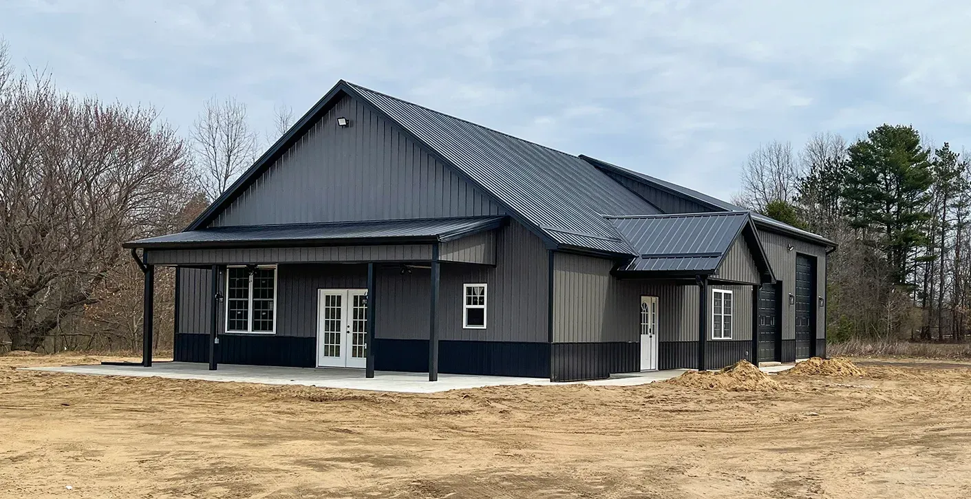 A small log cabin with a porch and a metal roof is sitting in the middle of a field.