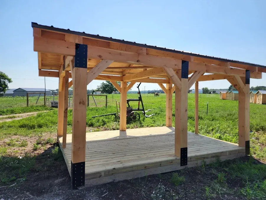 A wooden pavilion is sitting in the middle of a grassy field.