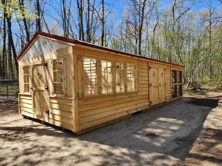 A wooden shed with a red roof is sitting in the middle of a forest.