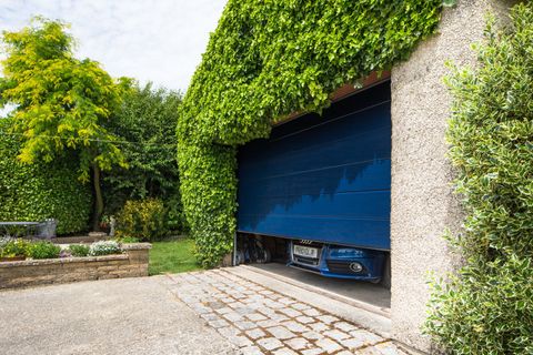 A garage covered in plants opening with a car exiting through an open garage door