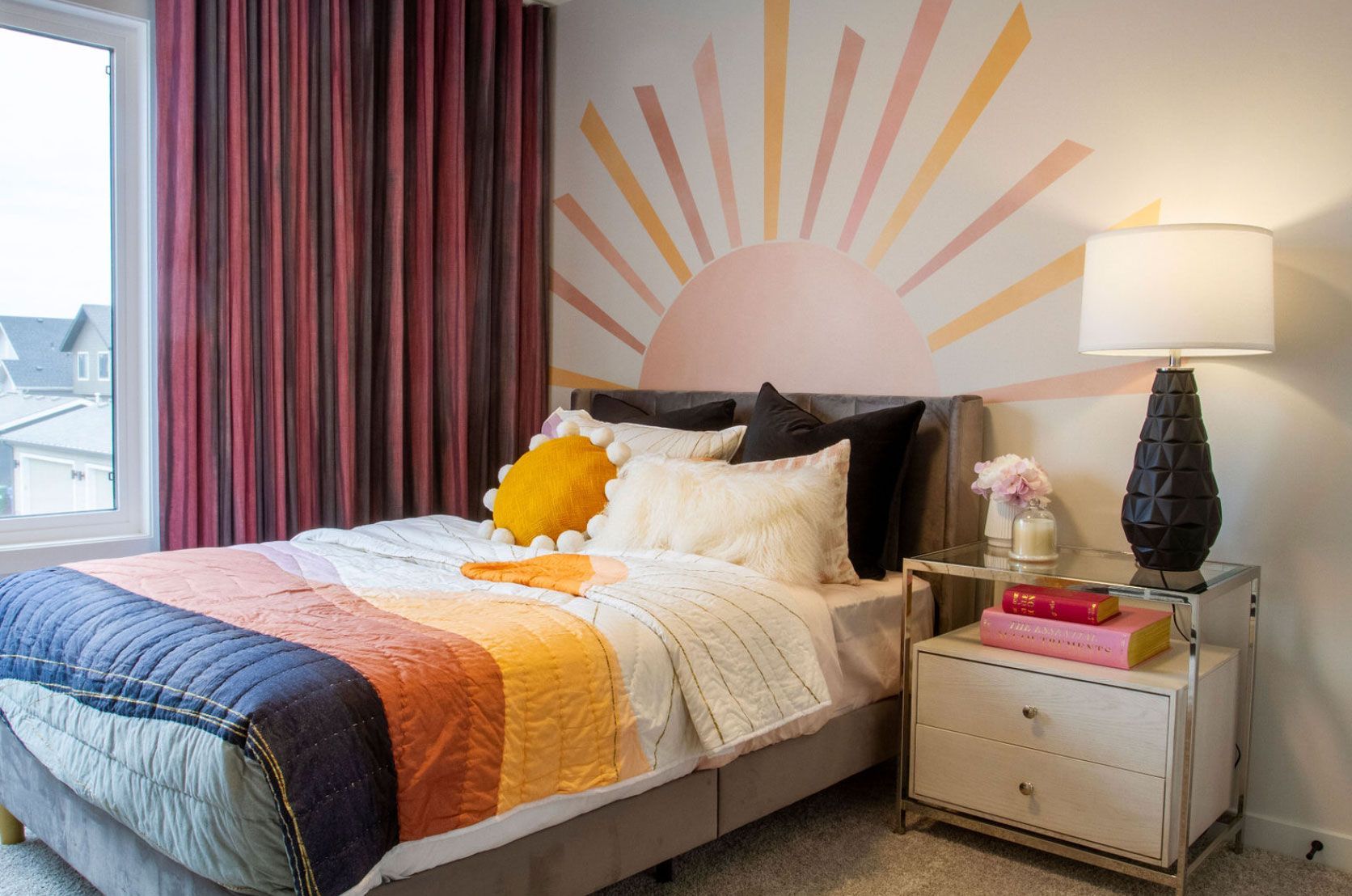 A bedroom with a bed , nightstand , lamp and a sun painted on the wall.