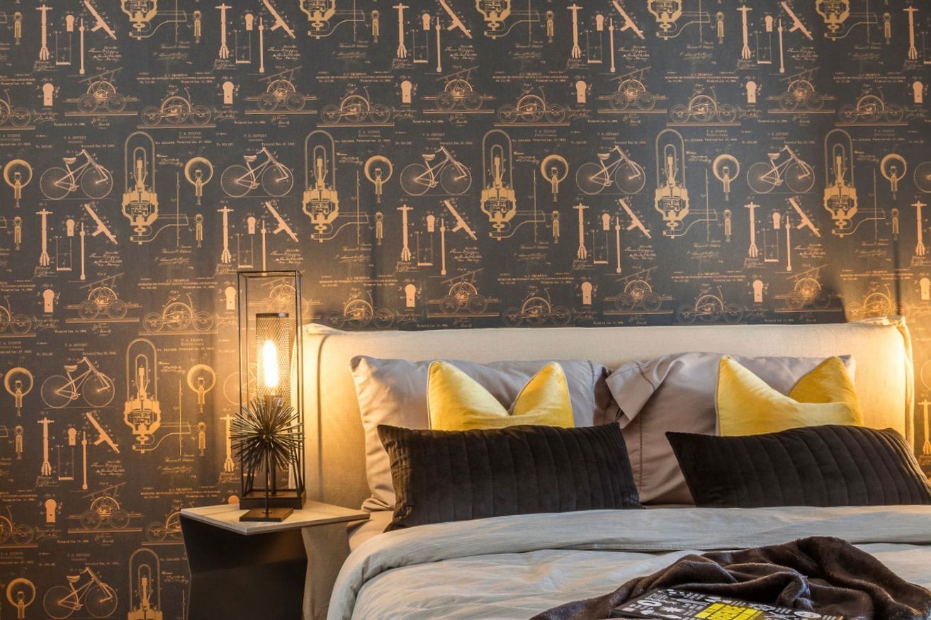 A bedroom with a bed , nightstand , lamp and wallpaper with keys on it.