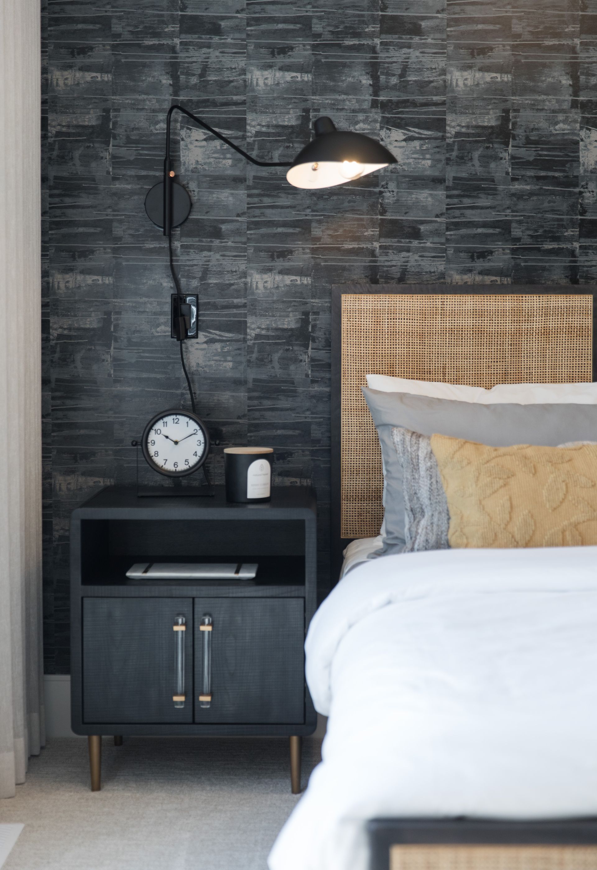 A bedroom with a bed , nightstand , clock and lamp.