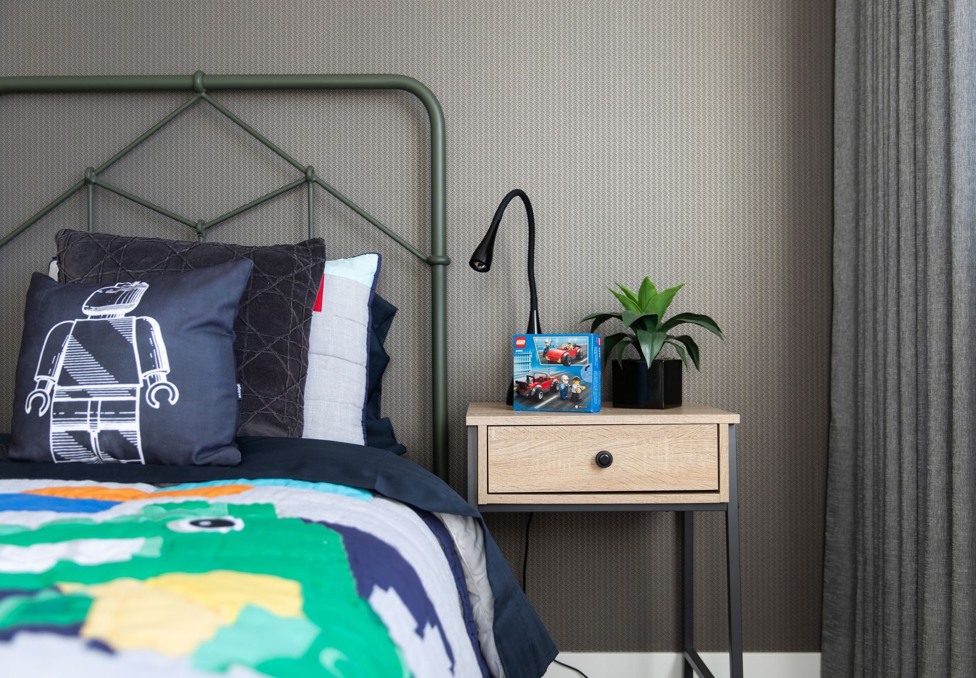 A bedroom with a bed , nightstand , lamp and plant.