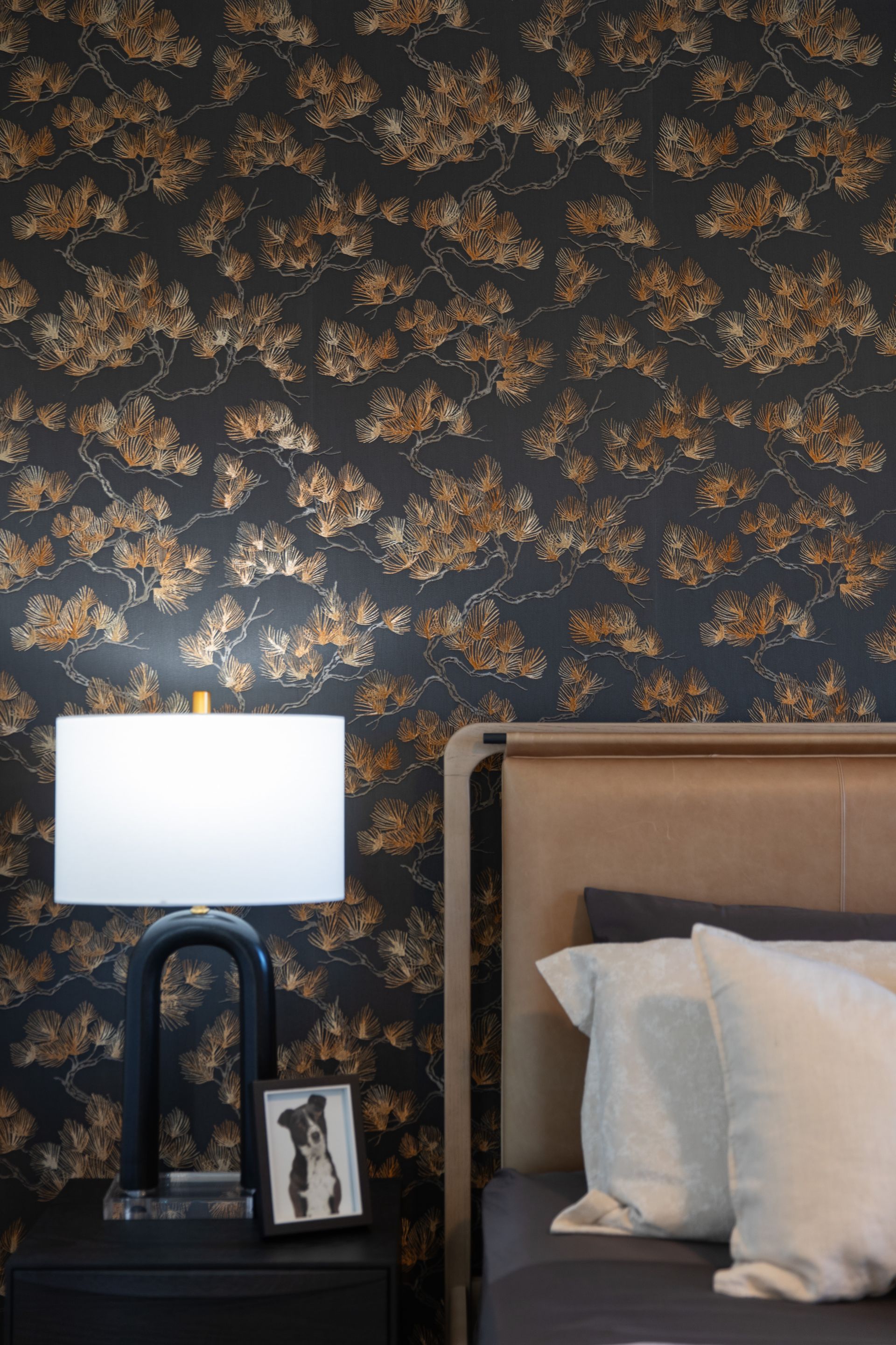 A bedroom with a bed , nightstand , lamp and floral wallpaper.