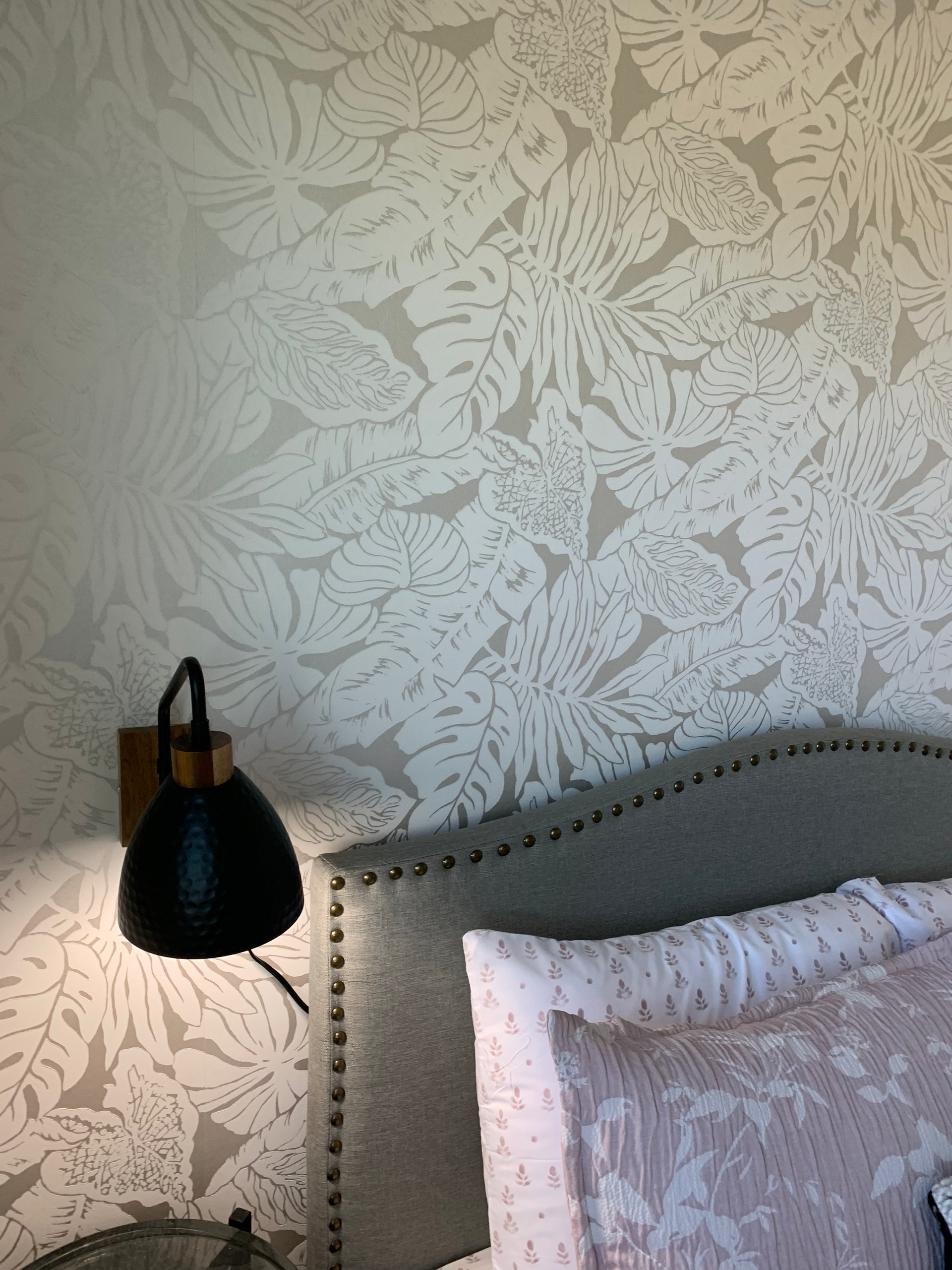A bedroom with a bed , nightstand , lamp and floral wallpaper.