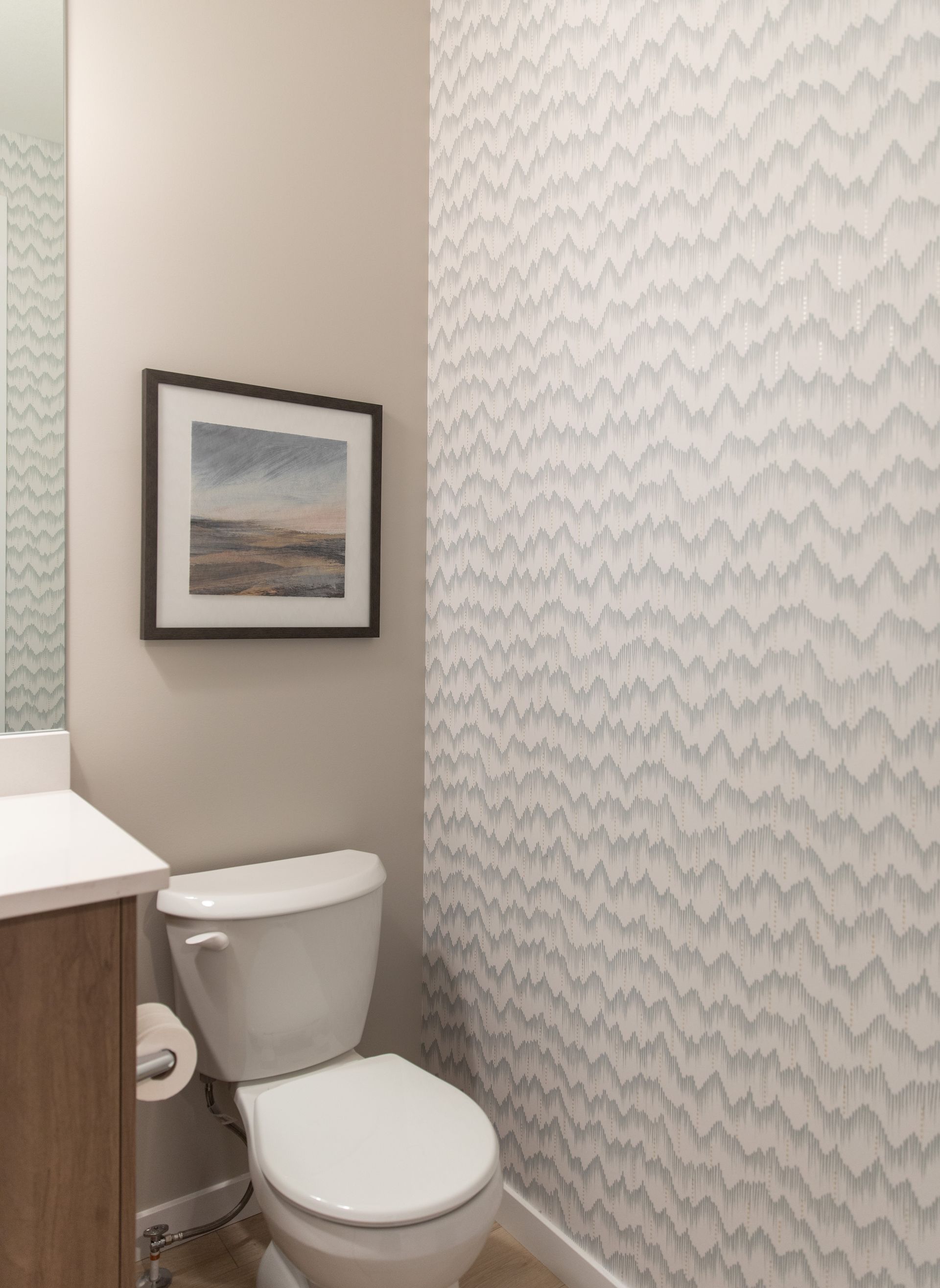 A bathroom with a toilet , sink , mirror and chevron wallpaper.