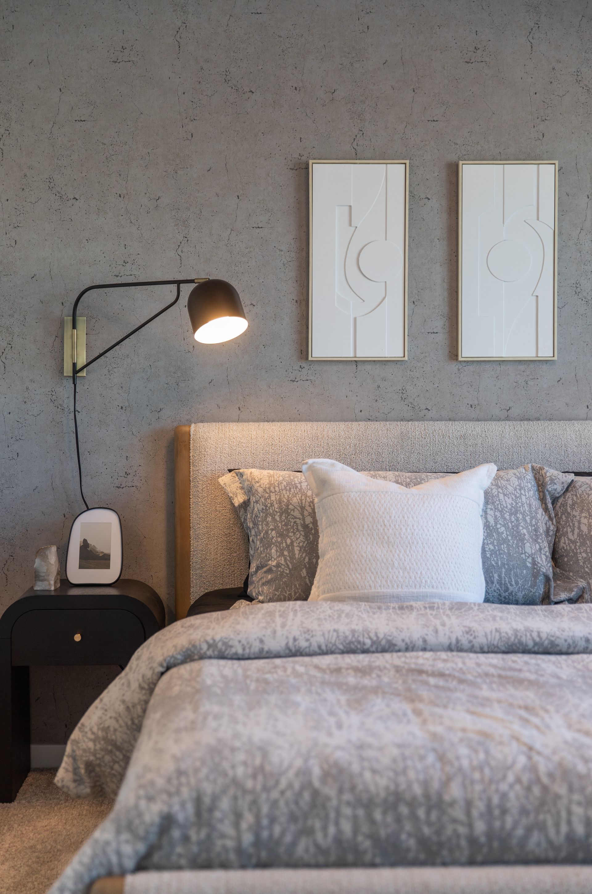 A bedroom with a bed , nightstand , lamp and two paintings on the wall.