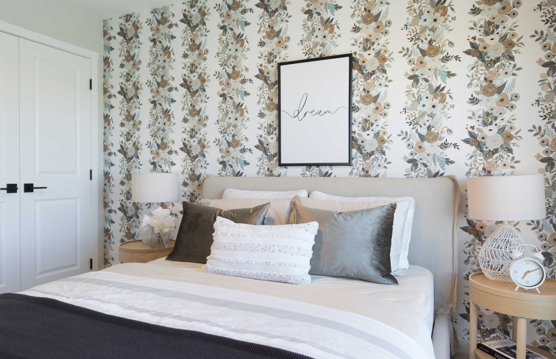 A bedroom with a bed , lamps , nightstands and a floral wallpaper.