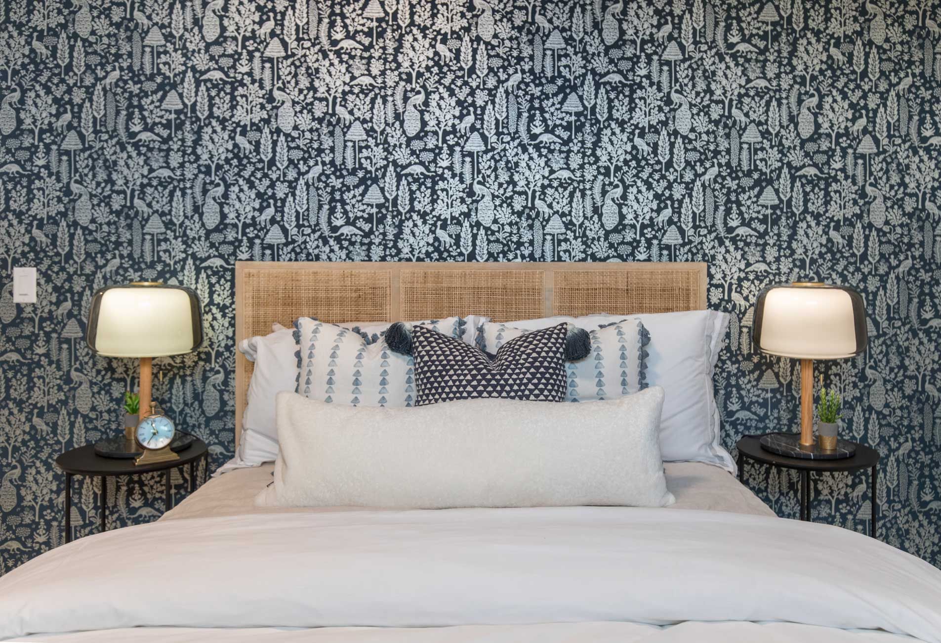 A bedroom with a bed , two lamps , and a patterned wall.