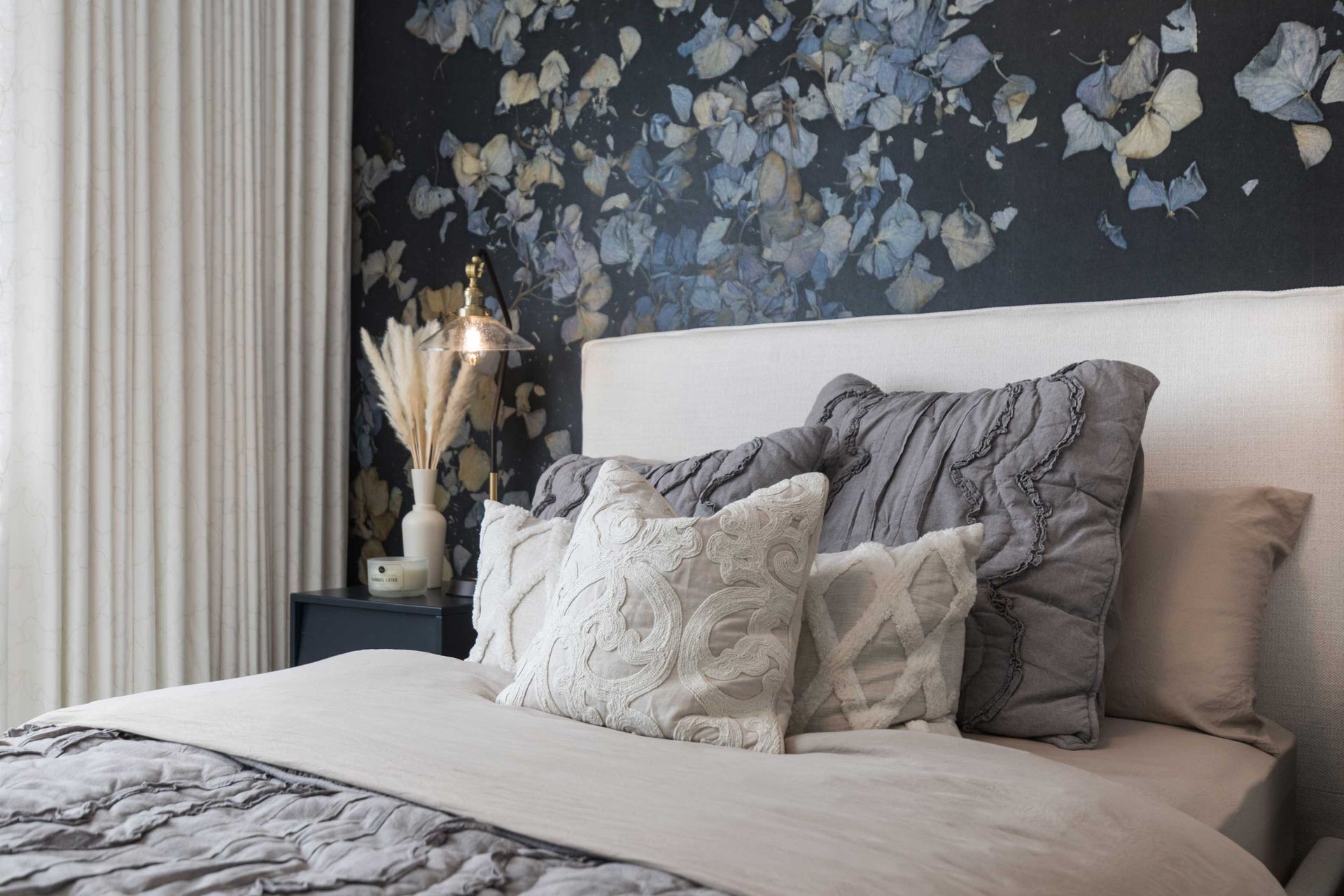 A bedroom with a bed , nightstand , and floral wallpaper on the wall.