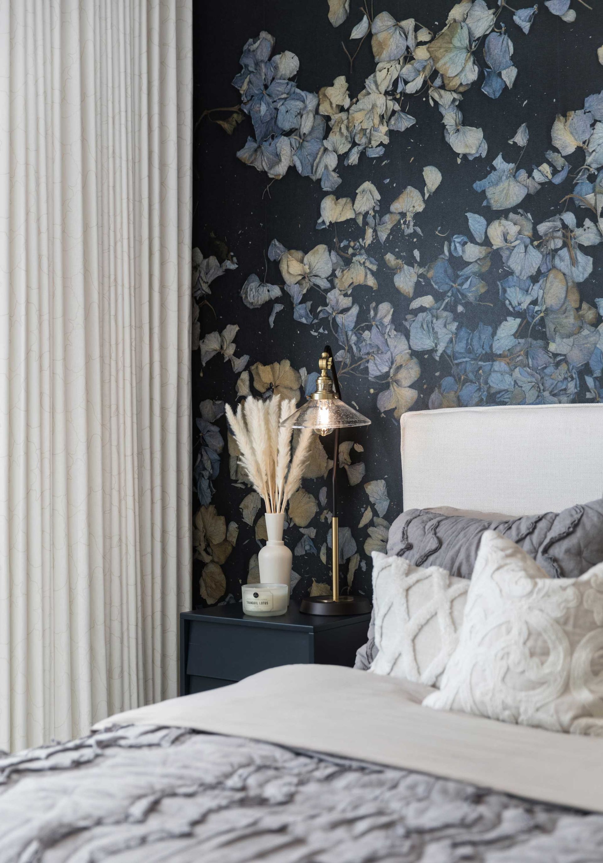 A bedroom with a bed , nightstand , lamp and floral wallpaper.