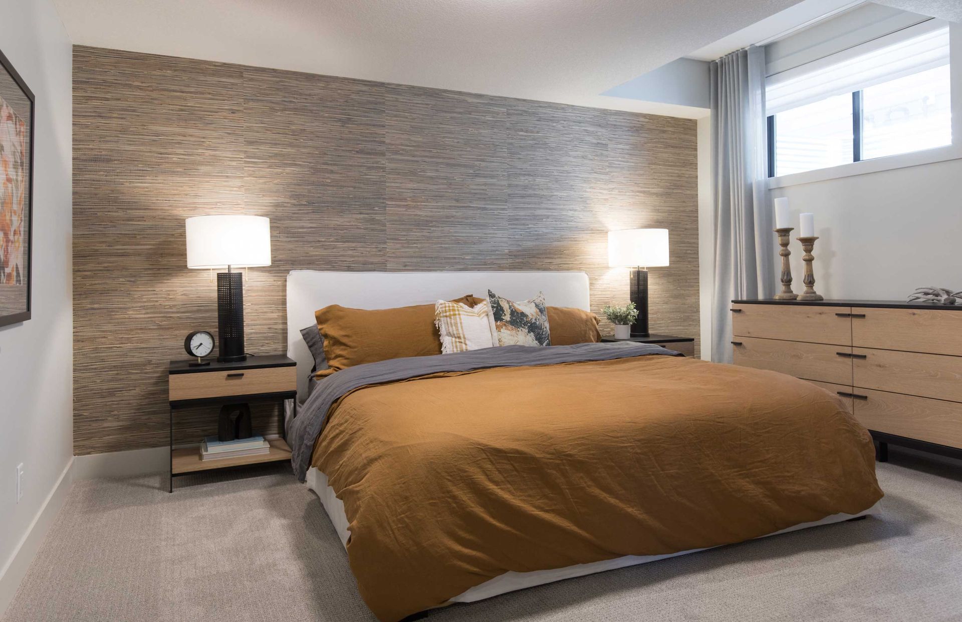 A bedroom with a large bed , dresser , nightstand and lamps.