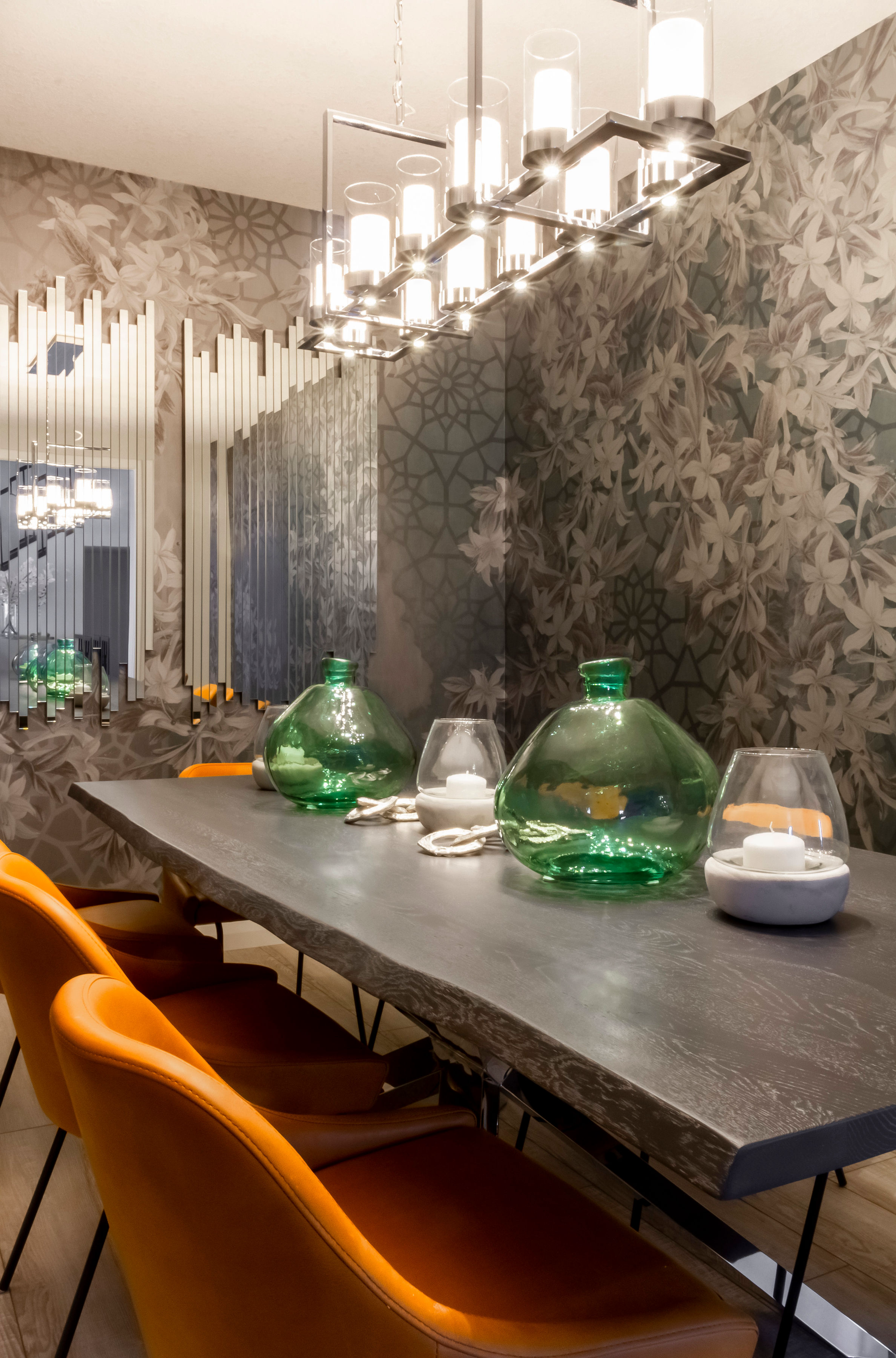 A dining room table with orange chairs and green vases on it