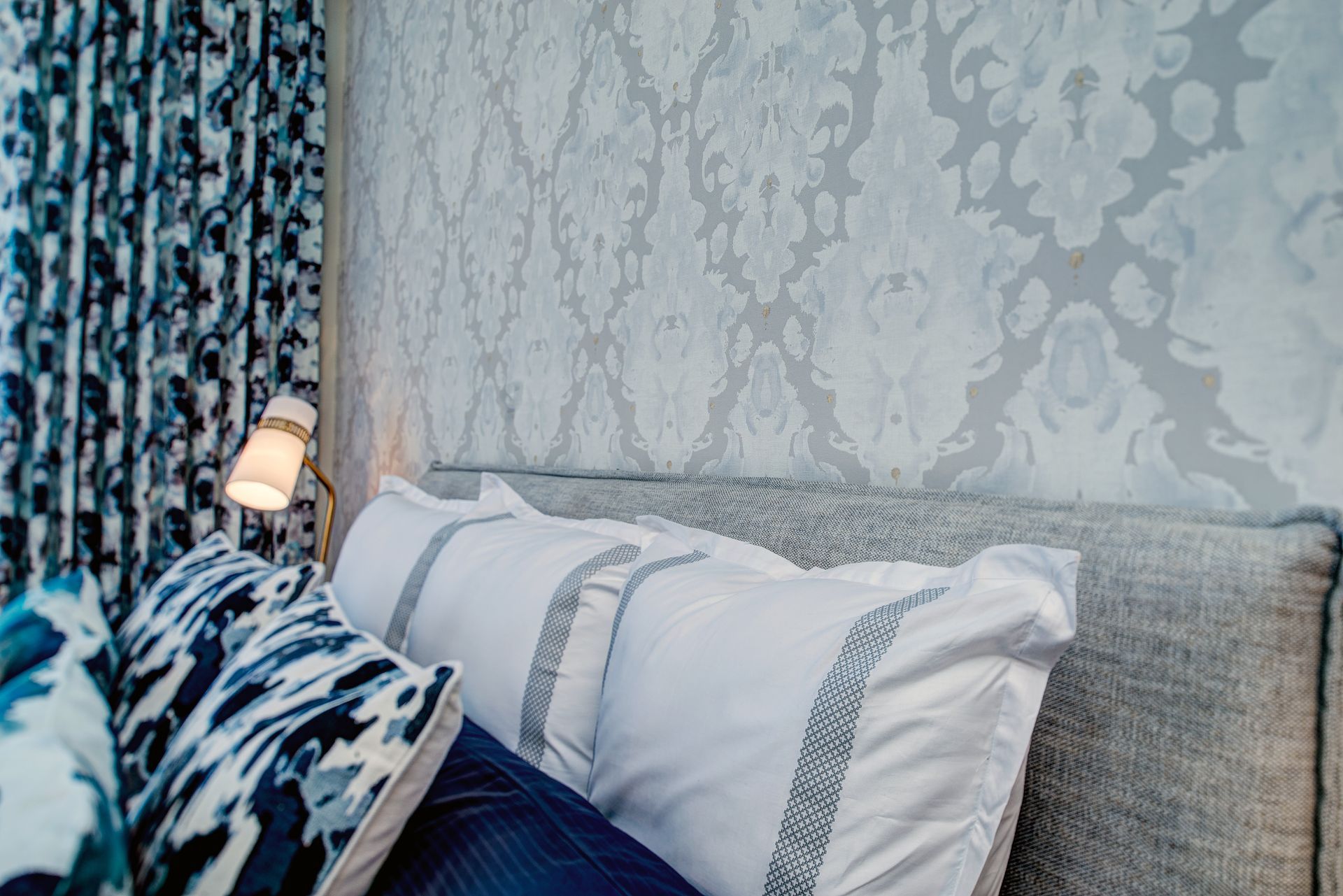 A bed with blue and white pillows and a lamp on the wall.