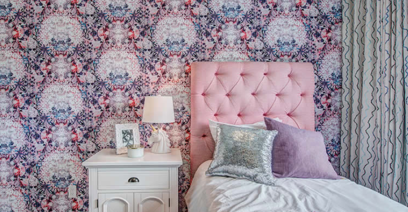 A bedroom with a bed , nightstand , lamp and floral wallpaper.