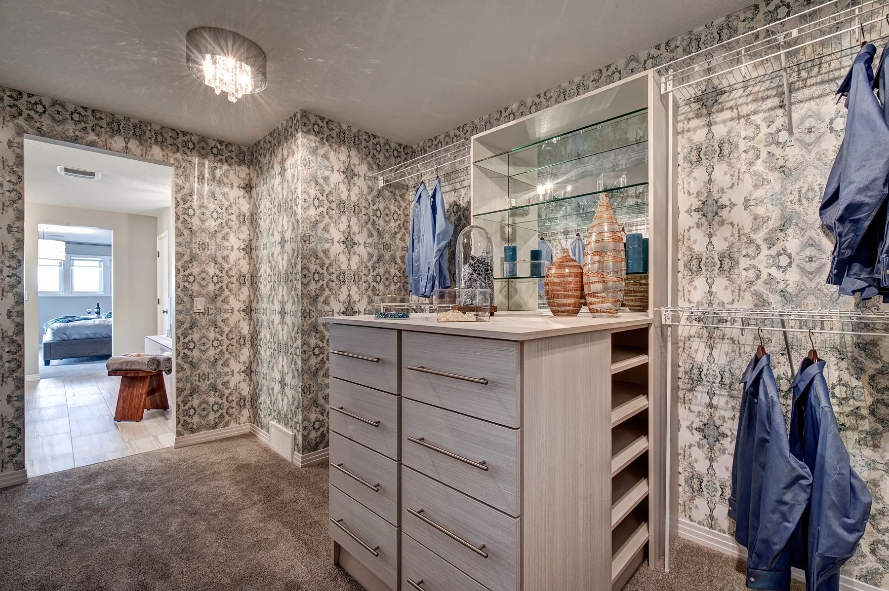 A walk in closet with lots of drawers and clothes hanging on the wall.