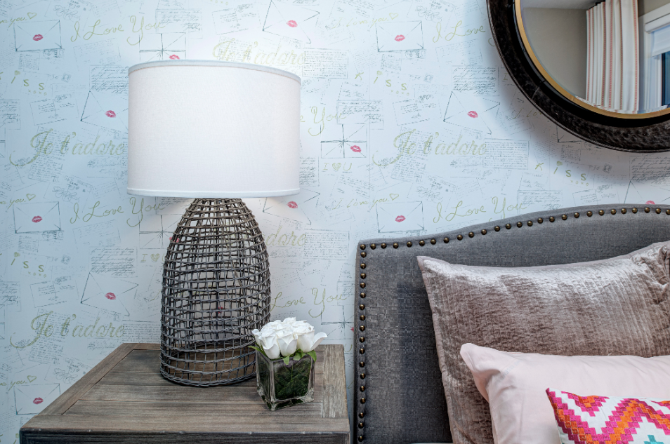 A bedroom with a bed , nightstand , lamp and mirror.