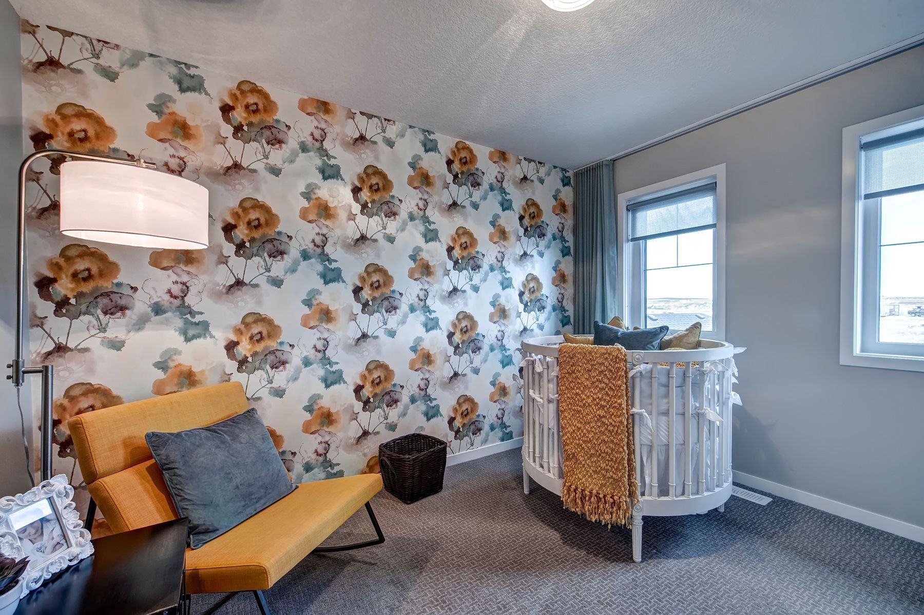 A nursery with a crib , chair , lamp and floral wallpaper.