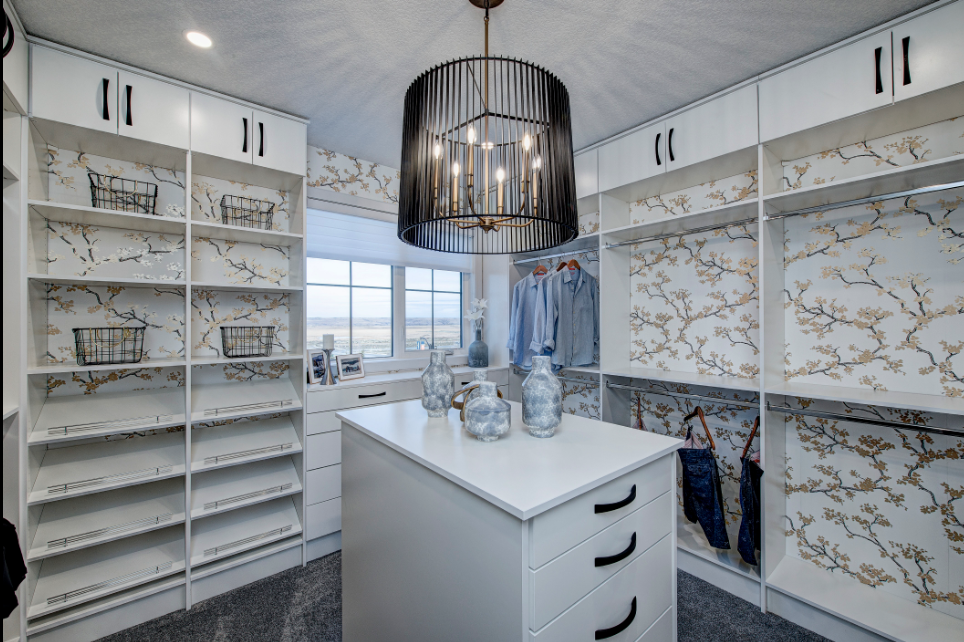 A walk in closet with a large island in the middle and a chandelier hanging from the ceiling.