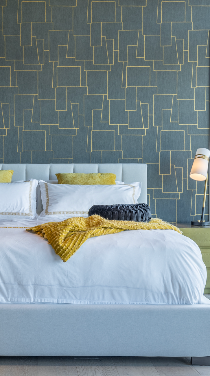 A bed with white sheets and yellow pillows in a bedroom with a blue wall.