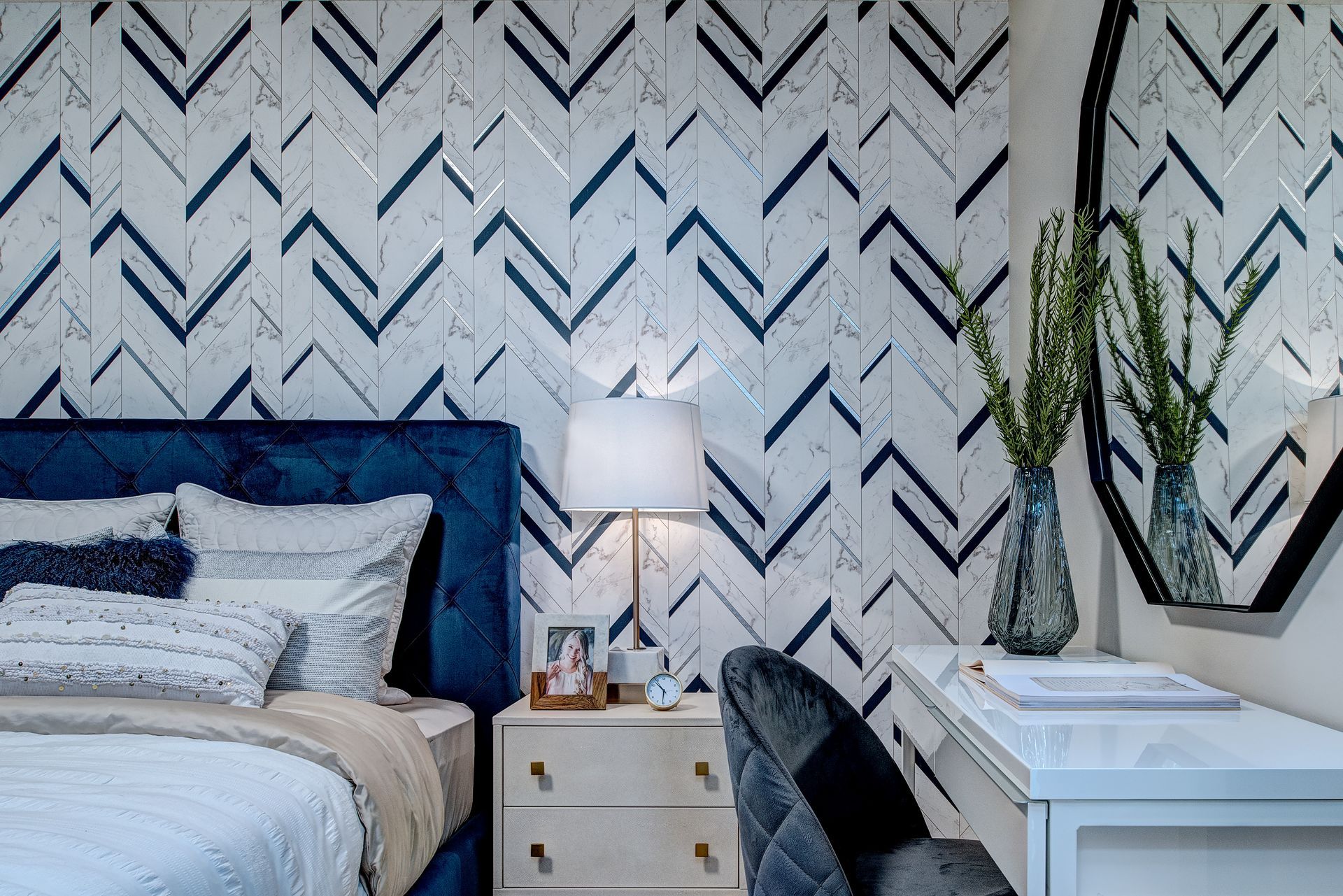 A bedroom with a bed , nightstand , desk and mirror.