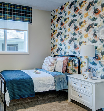 A bedroom with a bed , nightstand , lamp and floral wallpaper.