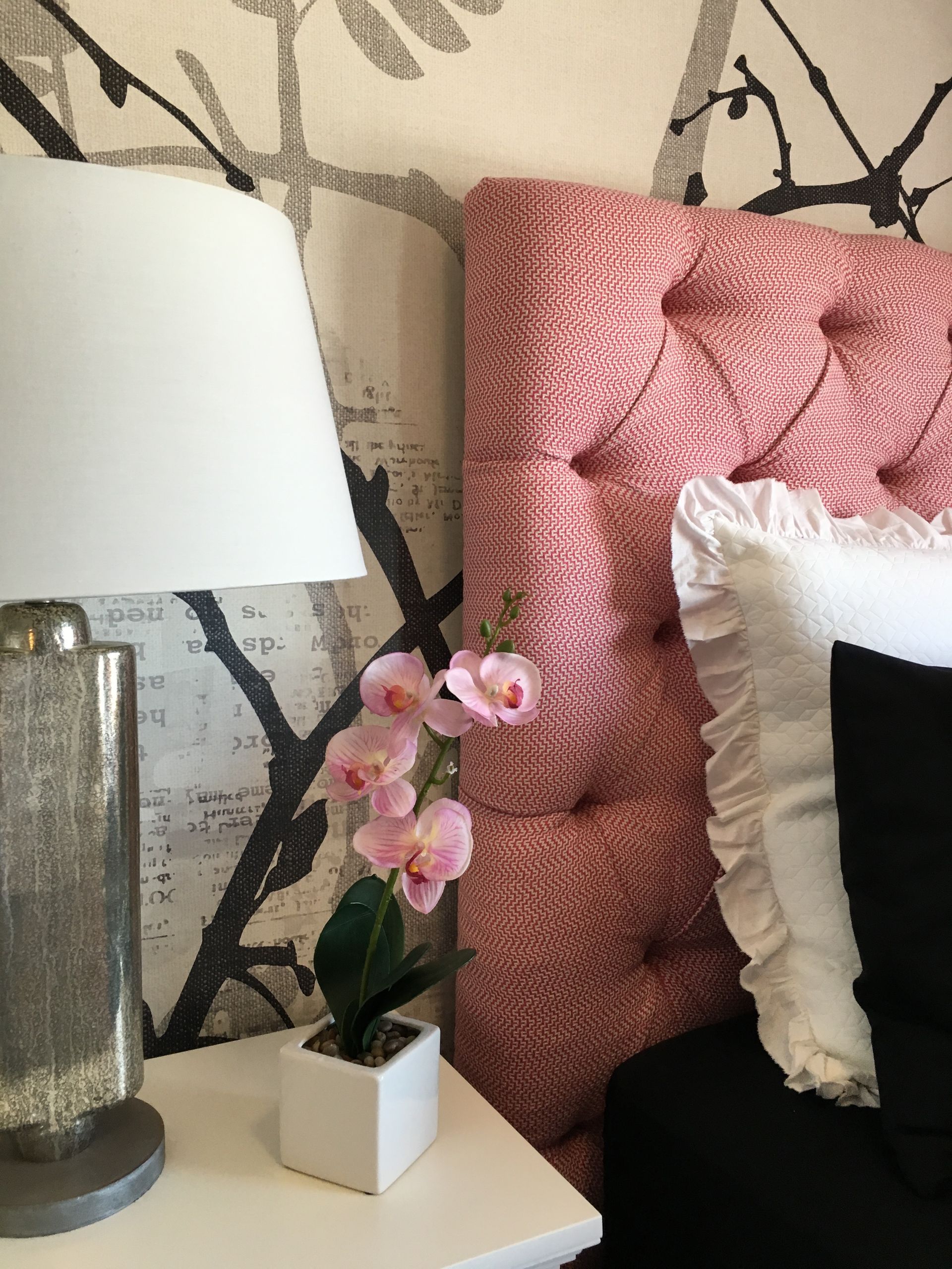 A lamp sits on a nightstand next to a bed with a pink headboard