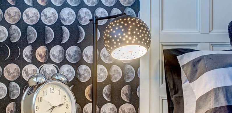 A clock is sitting on a nightstand next to a lamp in a bedroom.