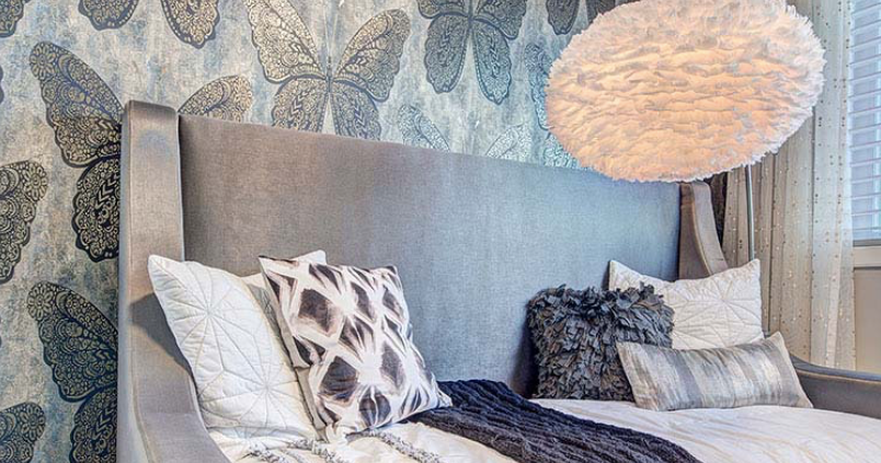 A bedroom with a bed , pillows , a lamp and a butterfly wallpaper.