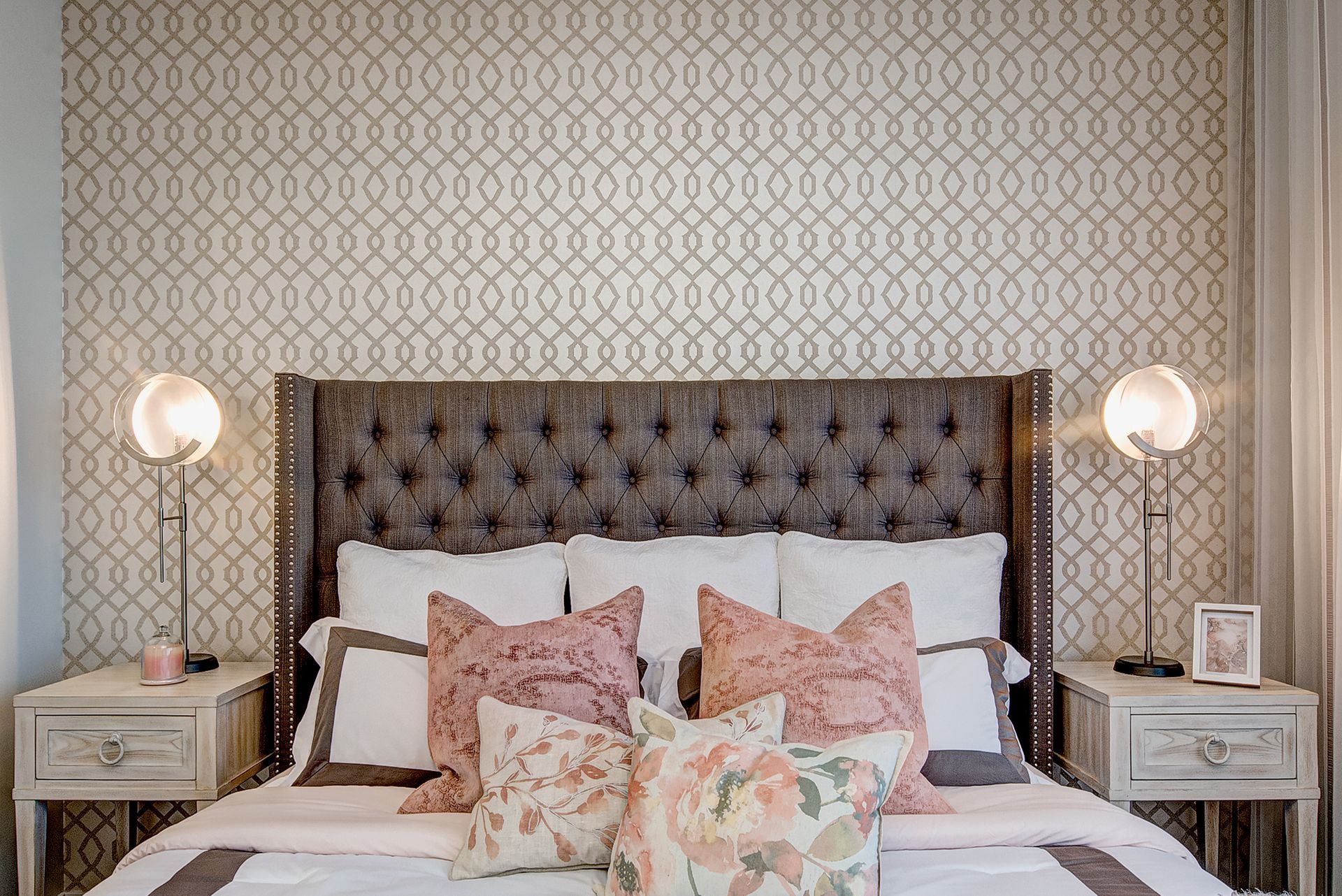 A bedroom with a bed , nightstands , lamps and a patterned wallpaper.