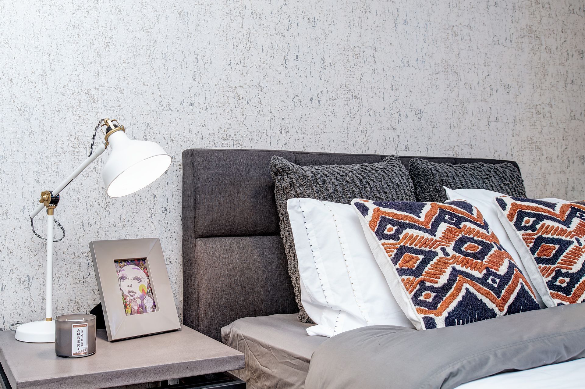 A bedroom with a bed , nightstand , lamp and picture frame.