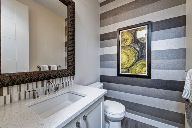 A bathroom with a sink , toilet , mirror and striped wall.