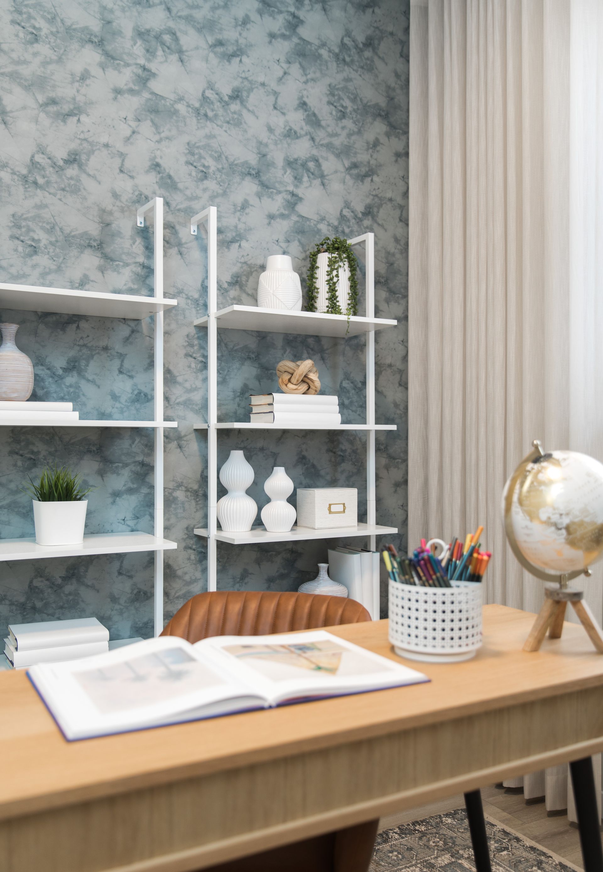 A home office with a desk , chair , shelves and a globe.