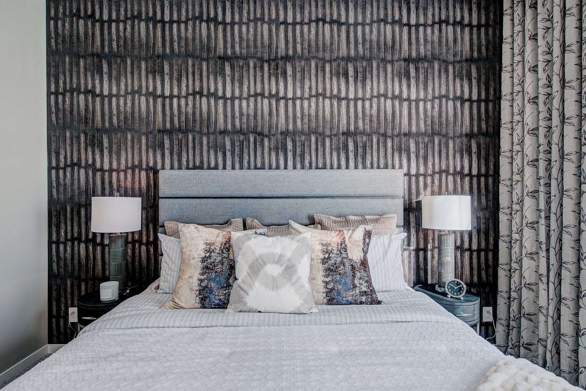 A bedroom with a bed , lamps , and a wall with a patterned wallpaper.