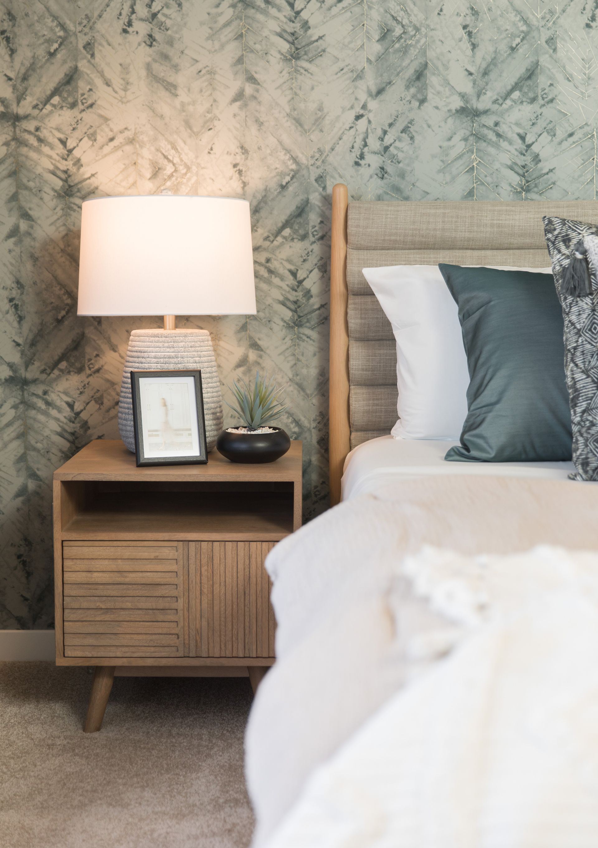 A bedroom with a bed , nightstand , lamp and picture frame.