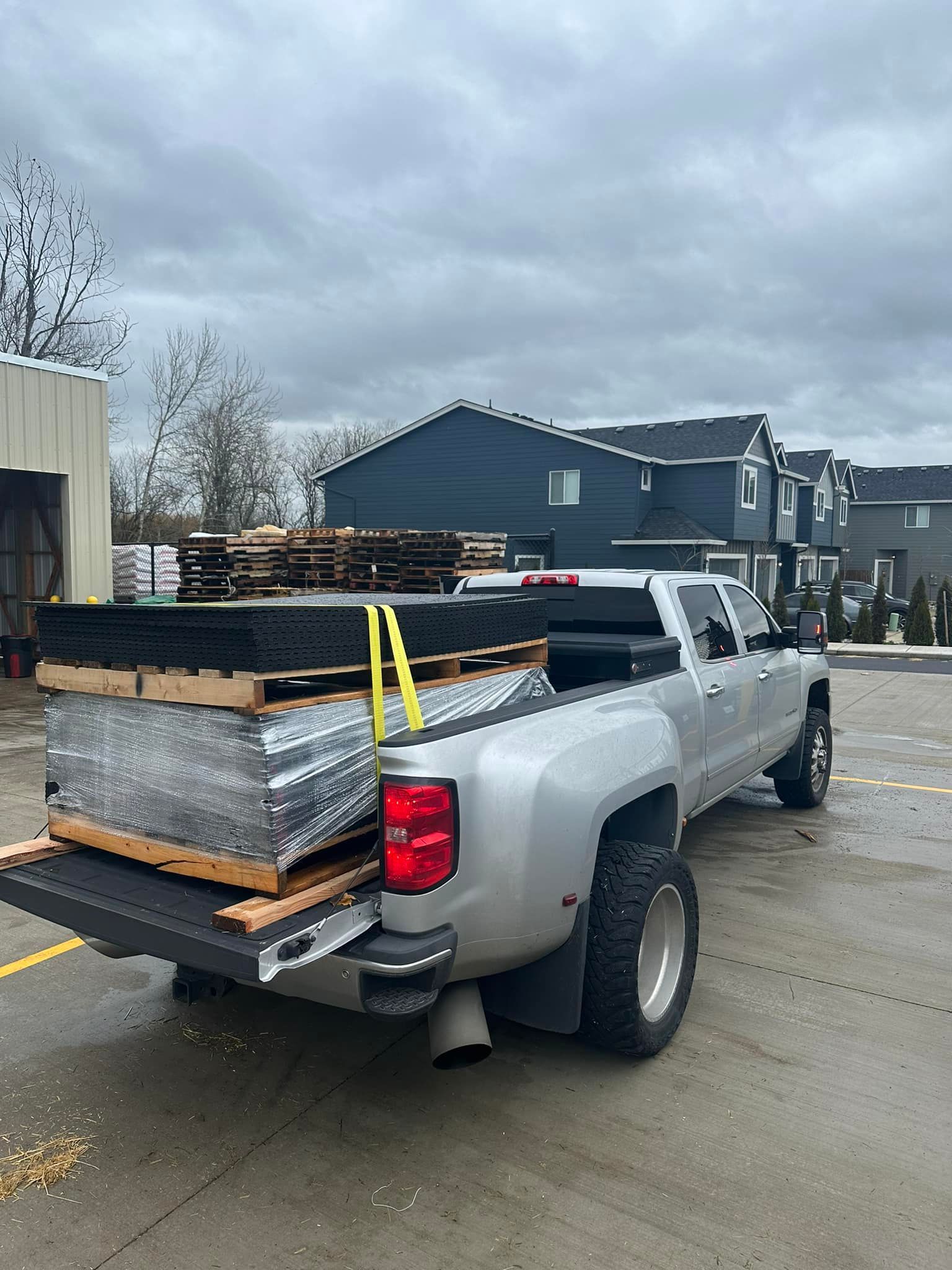 A silver truck is parked in a parking lot with pallets in the back.