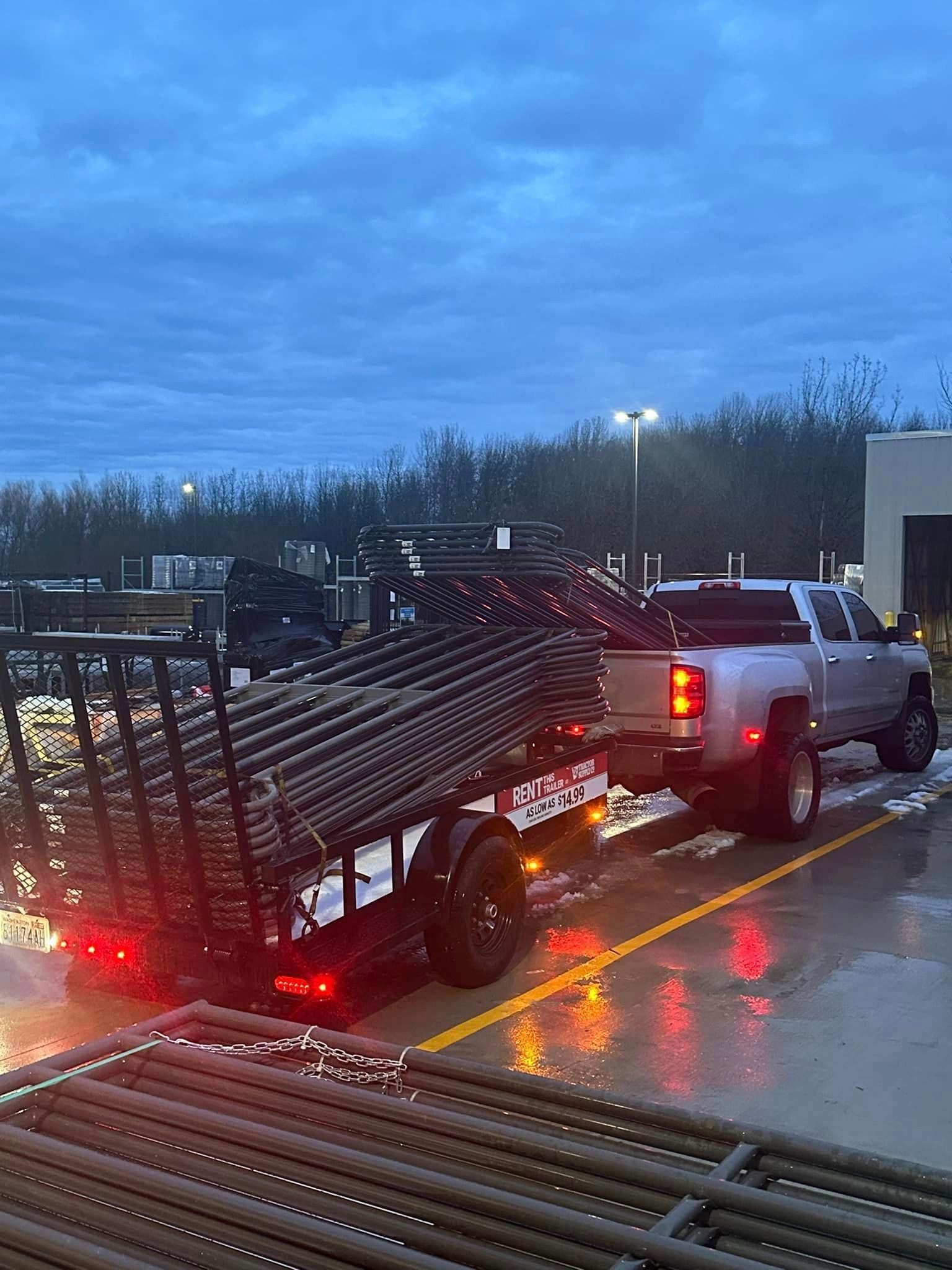 A truck is pulling a trailer full of pipes in a parking lot.