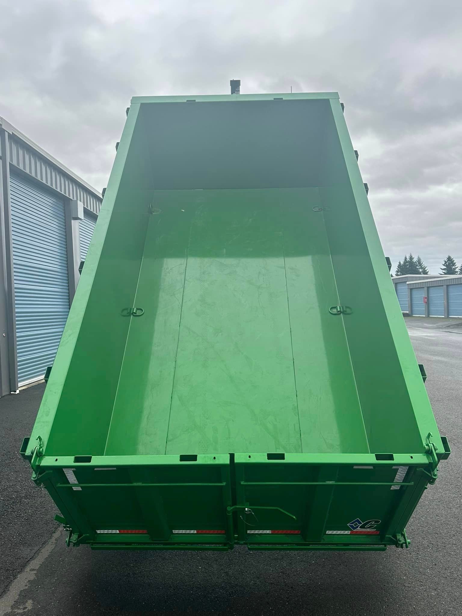 A green dumpster is parked in front of a building.