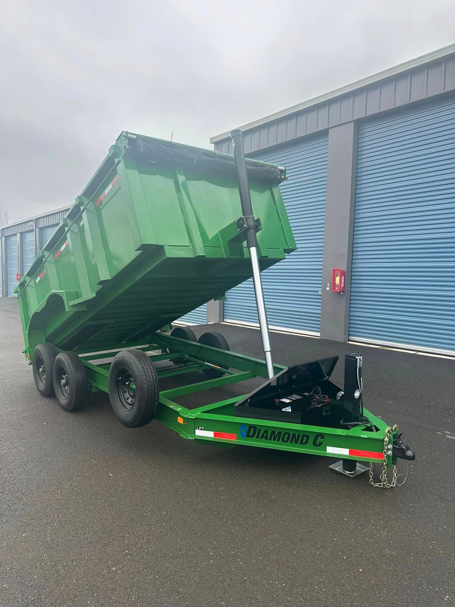 A green dump trailer is parked in front of a building.