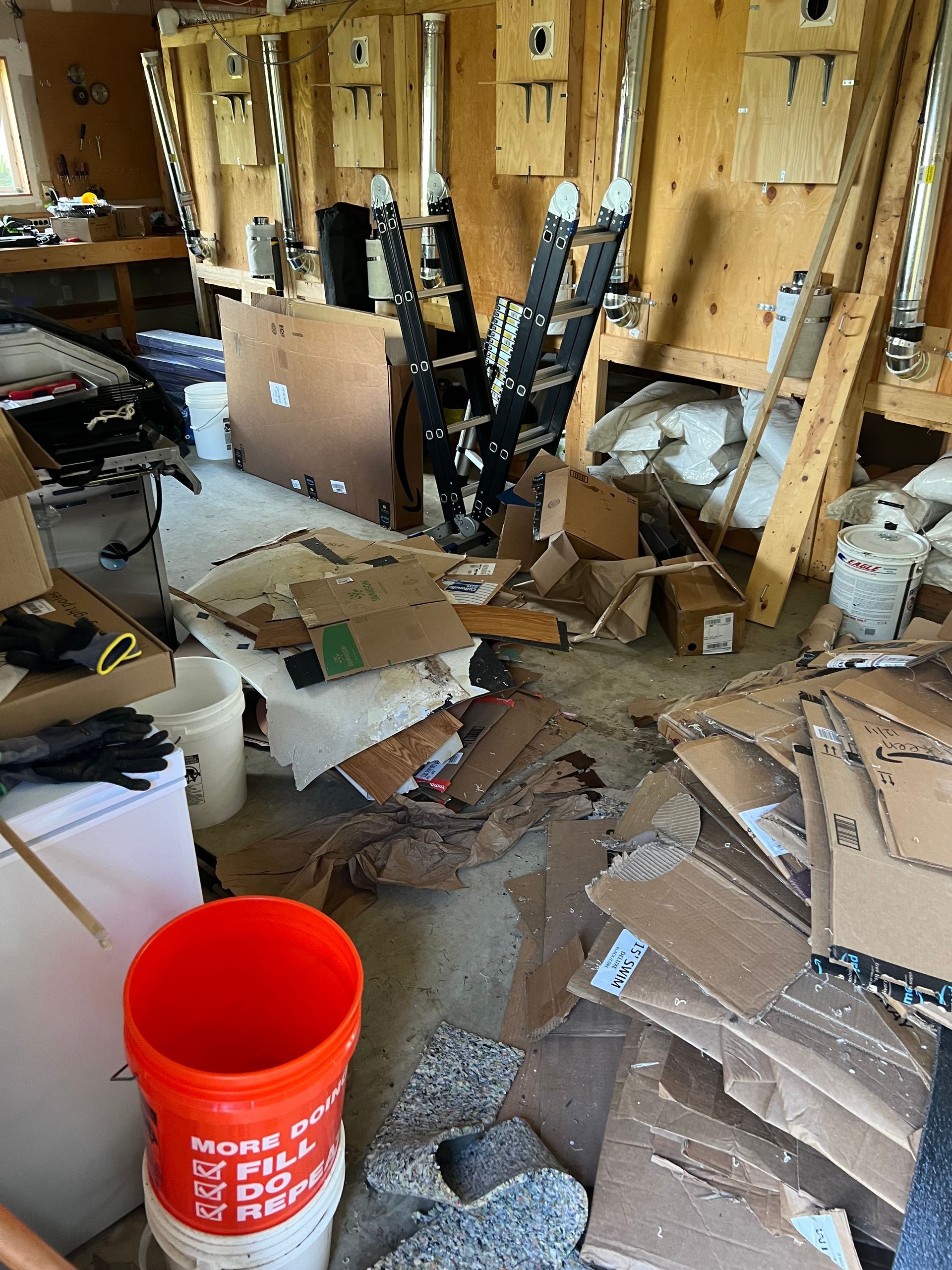 A room filled with lots of cardboard boxes and a red bucket.