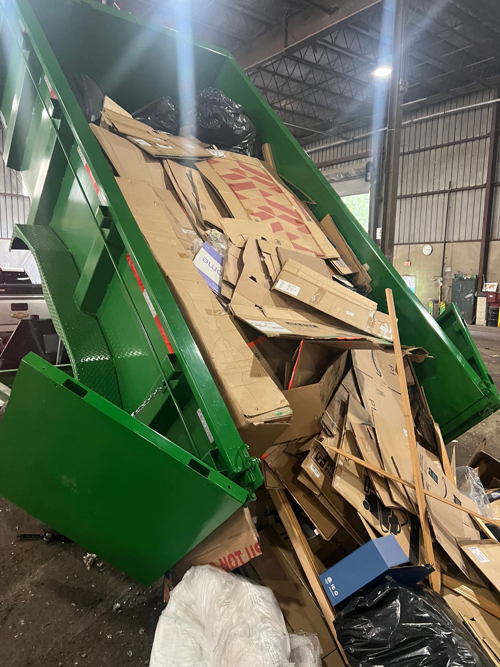 A green dumpster filled with cardboard boxes in a warehouse.